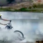 バイクのタイヤ部分に板をつけてジェットスキーのように川を渡る映像。