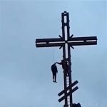 巨大な十字架に吊るされた男性の死体映像。