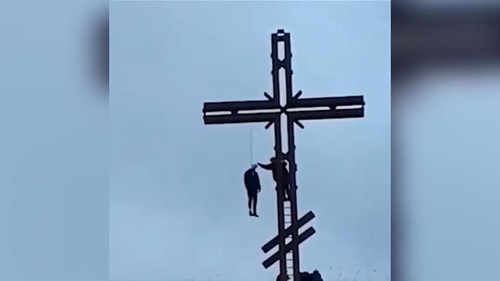巨大な十字架に吊るされた男性の死体映像。