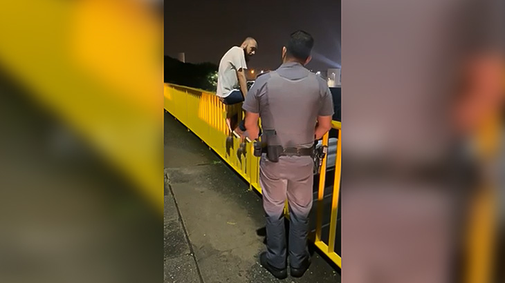 橋から身を投げようとする男を助け出して慰める警察官の映像。