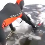 氷を割って水中から男性の死体を引き上げる映像。